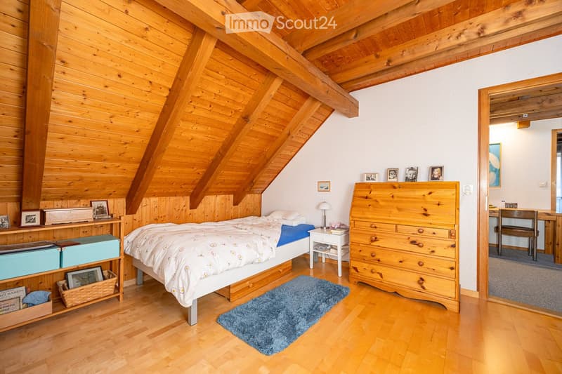 bedroom with wooden walls, bed, wooden dresser, wooden shelf, blue rug, lamp, nightstand