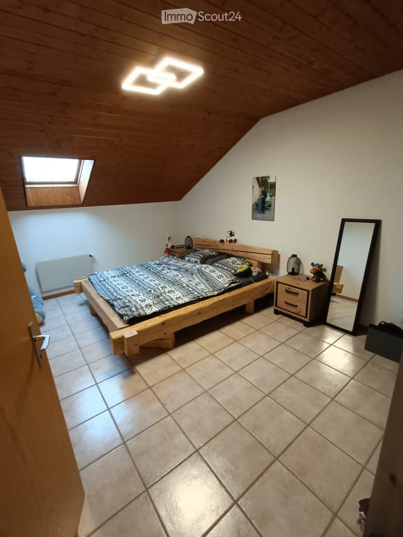 Cozy attic bedroom with wooden bed, nightstand, mirror, and skylight window.
