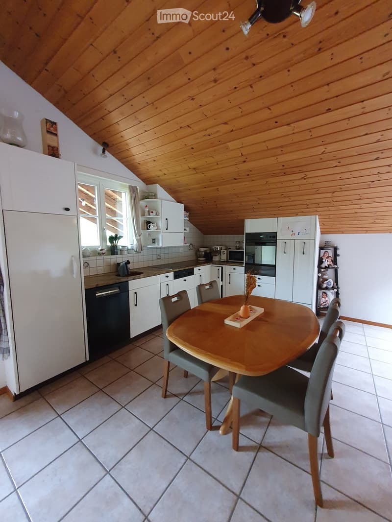 Bright kitchen with white cabinets, wooden ceiling, tiled floor, and a round wooden dining table with four chairs.
