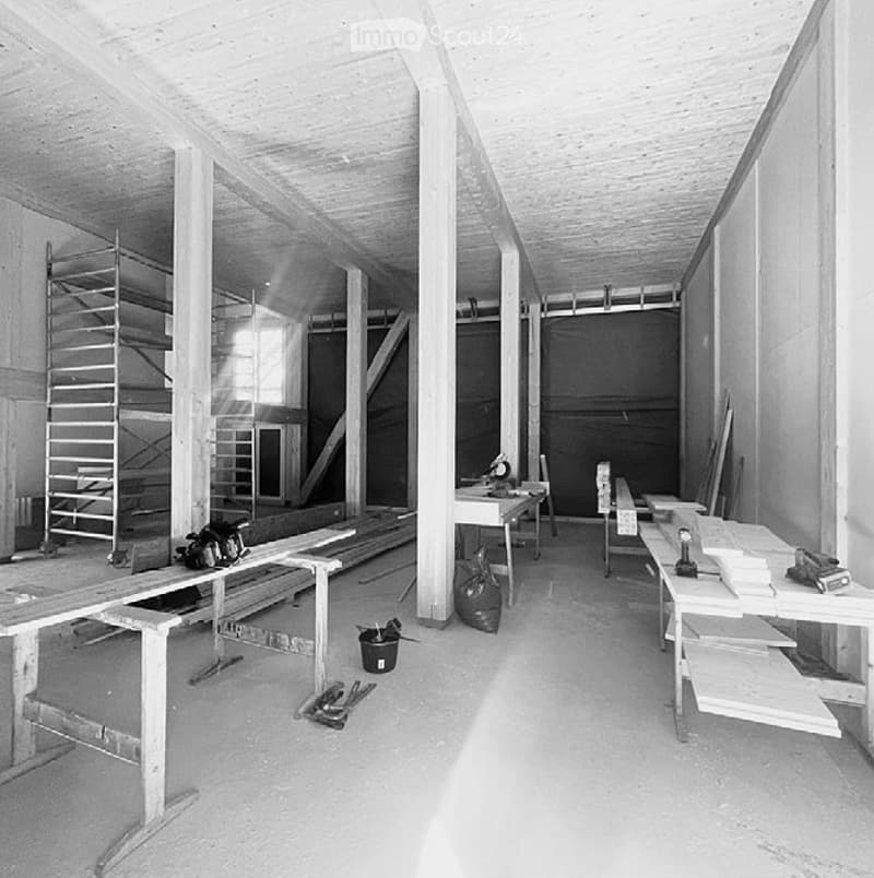 Empty workshop or construction space with exposed wooden beams, concrete walls, and various construction tools and materials scattered around.