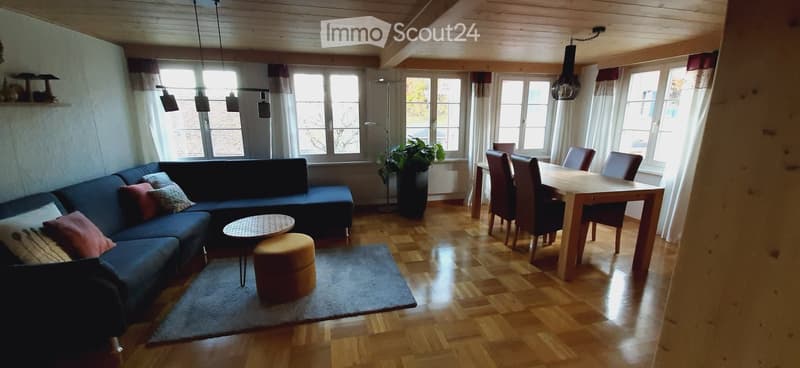 Dining room with large windows and view, wooden floor, dining table with chairs, sofa with pillows, coffee table, potted plant