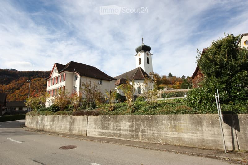 church with tower and spire, white exterior, brown roof, red shutters, concrete retaining wall