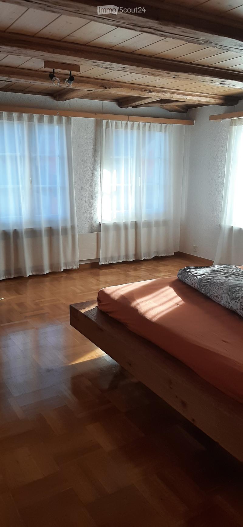 a room with wooden floor, bed, white curtains, radiator