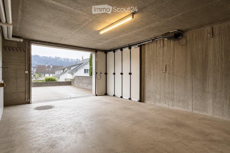 Empty garage with concrete walls and floor, large sliding doors, and a view of the outside area.