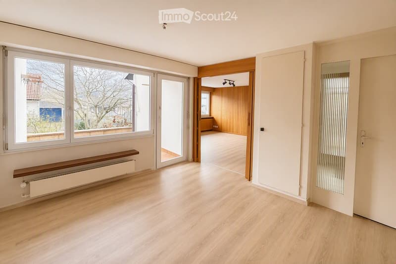 Empty room with light wooden flooring, large windows, and a radiator. No furniture or equipment is present.