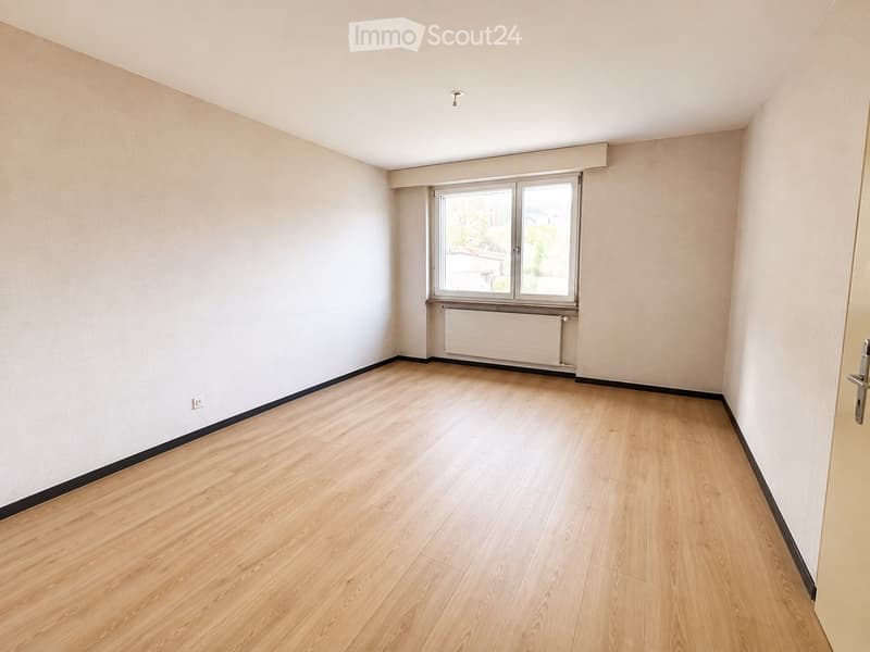 Empty room with light wooden flooring, white walls, and a window with a radiator below it.
