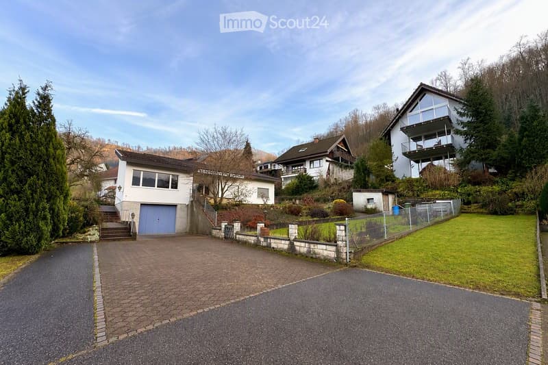 A residential area with multiple houses, including a two-story house with a garage, a raised ground floor, and a well-maintained garden.