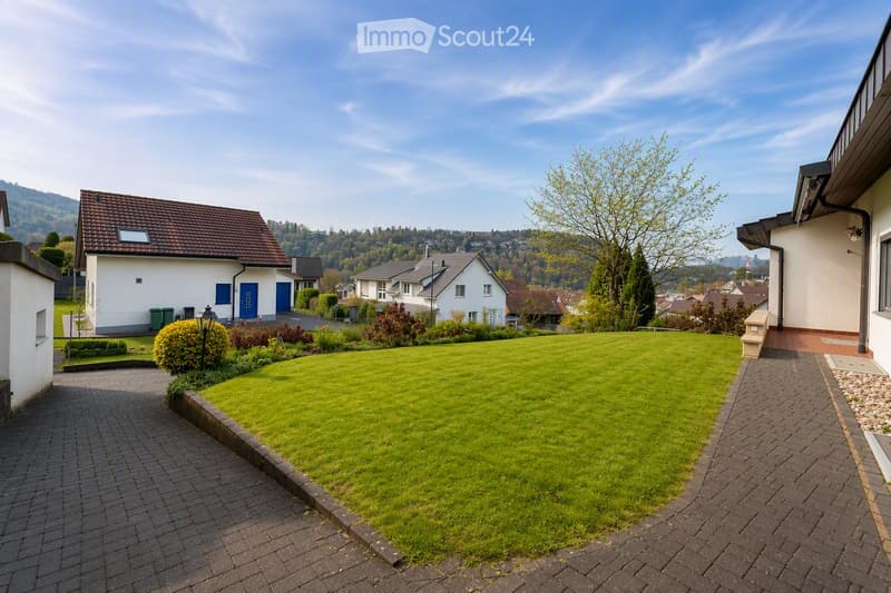 Well-maintained garden with a neatly trimmed lawn, a brick pathway, and surrounding houses with white walls and dark roofs.