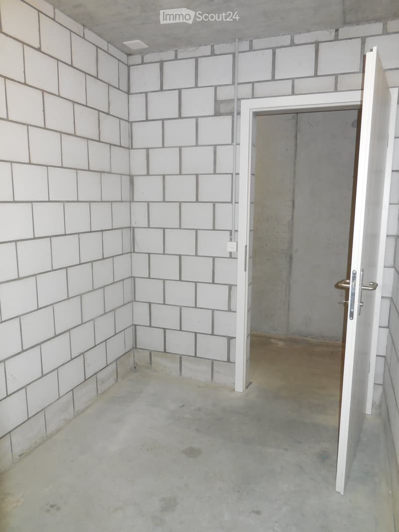 Empty room with white tiled walls and a concrete floor, featuring an open doorway leading to another space.