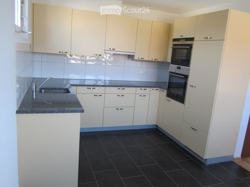 Modern kitchen with light-colored cabinets, dark tiled floor, granite countertop, and built-in oven.