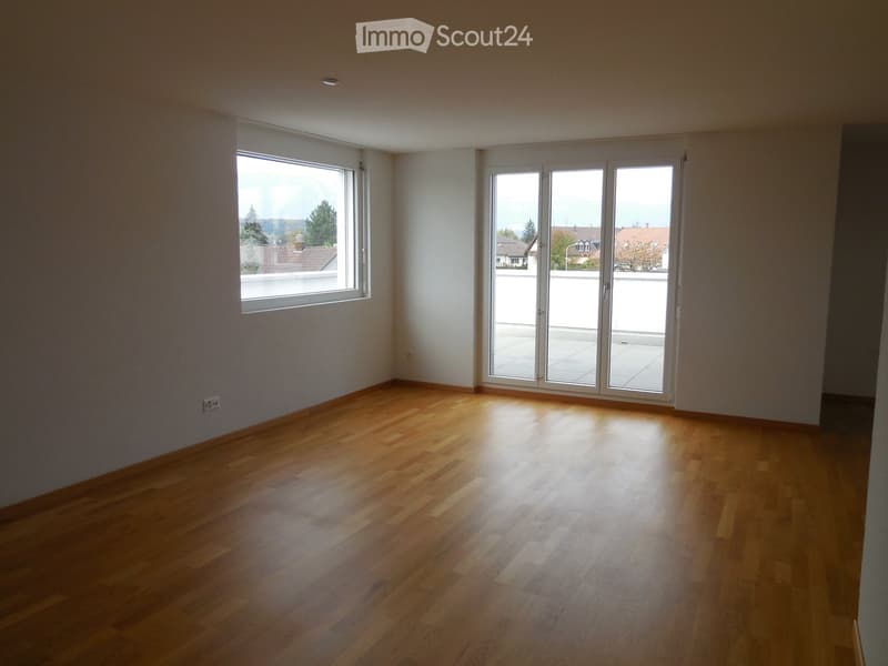 Empty room with wooden flooring, large windows, and sliding glass doors leading to a balcony.