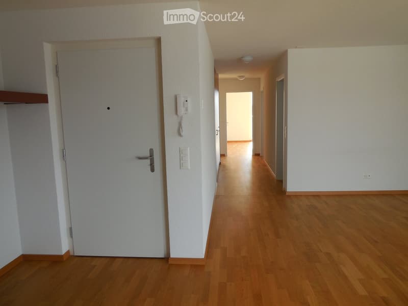 Empty hallway with wooden flooring, white walls, and a closed door on the left side.