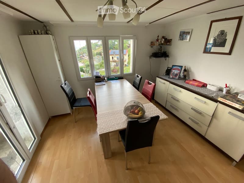 Dining room with a wooden dining table, chairs, a refrigerator, and a small kitchen area with cabinets and a countertop.