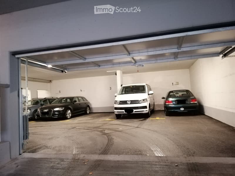 Interior of an underground parking garage with numbered stalls and parked cars.