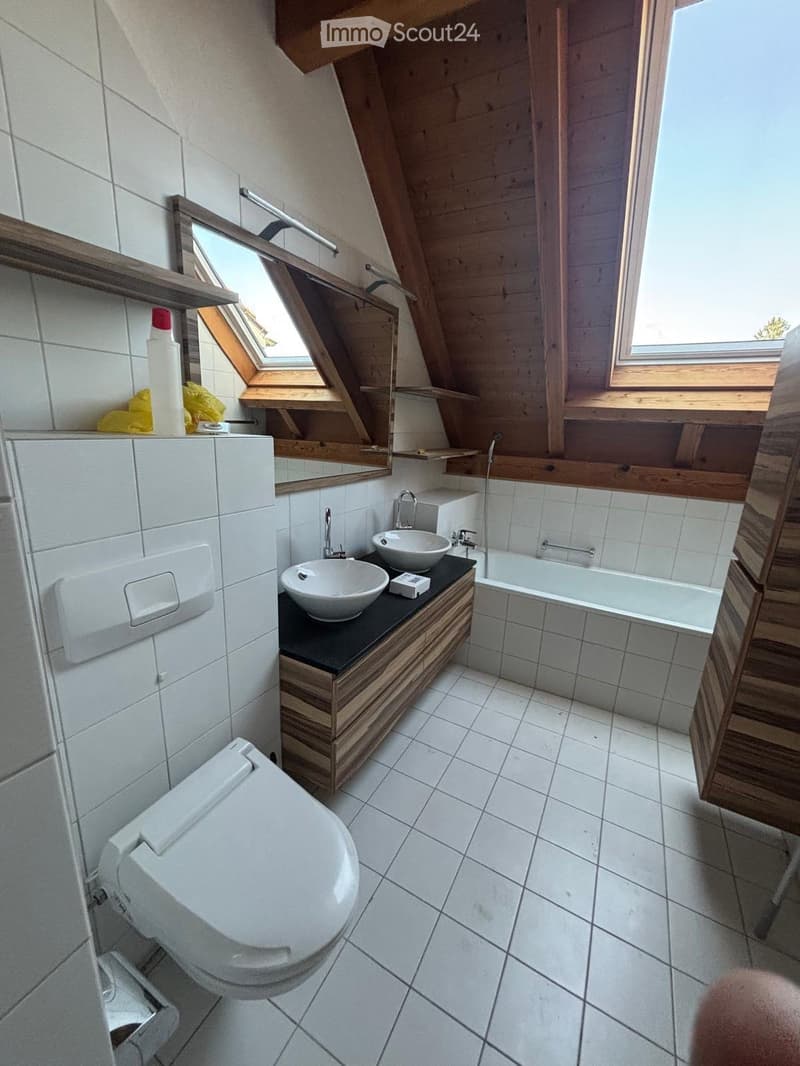 Modern bathroom with white tiles, a toilet, double sink vanity, bathtub, and skylight windows.