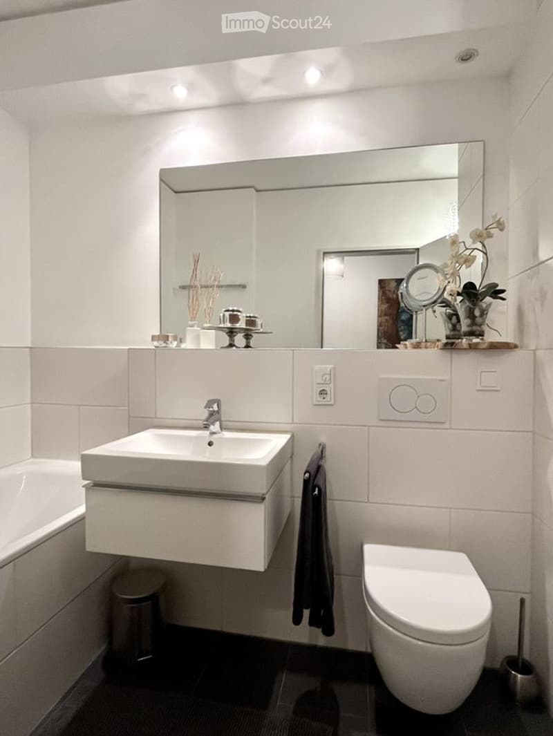 Modern bathroom with a white sink, large mirror, toilet, bathtub, and decorative items on the counter.