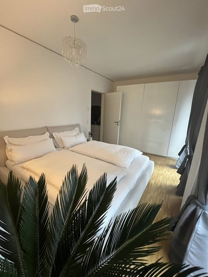 Modern bedroom with a large double bed, white pillows, a wardrobe, and a chandelier.