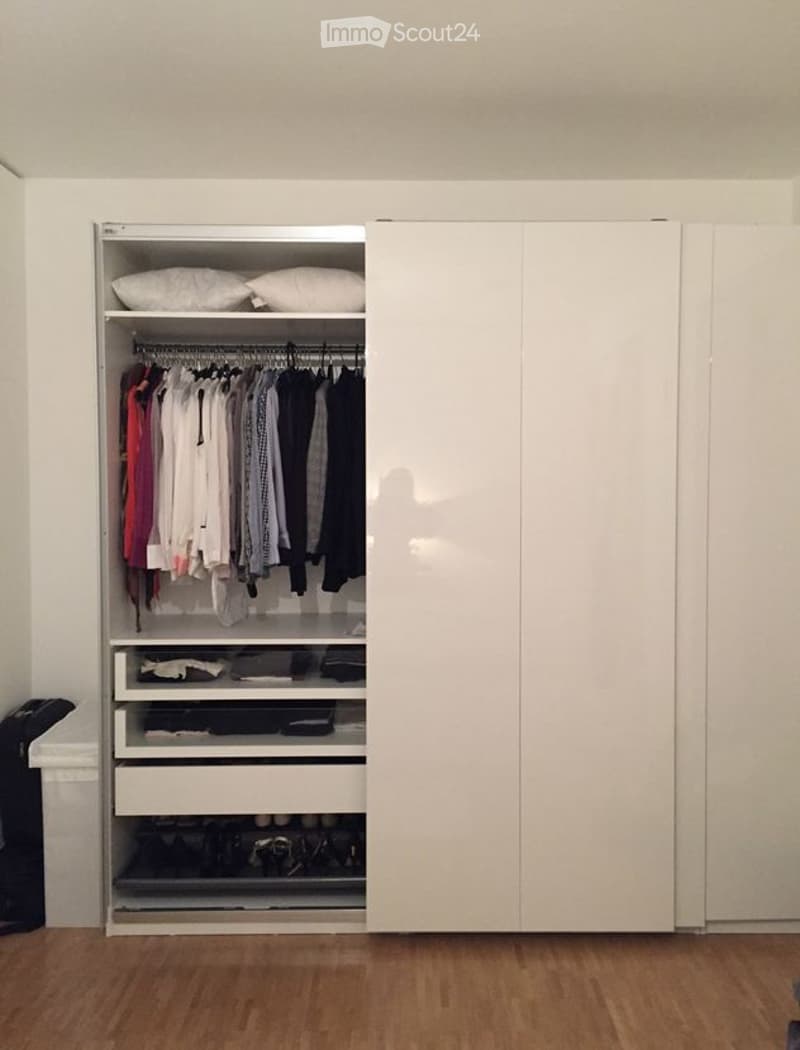 A modern, minimalist walk-in closet with white sliding doors, neatly organized clothes, and multiple storage compartments including drawers and shelves.