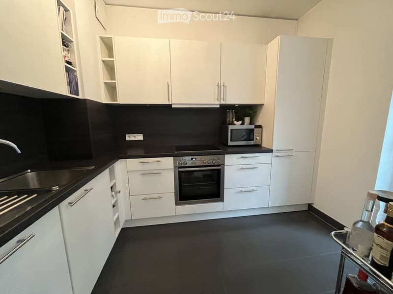 Modern kitchen with white cabinets, black countertops, stainless steel appliances, and a dark tiled floor.