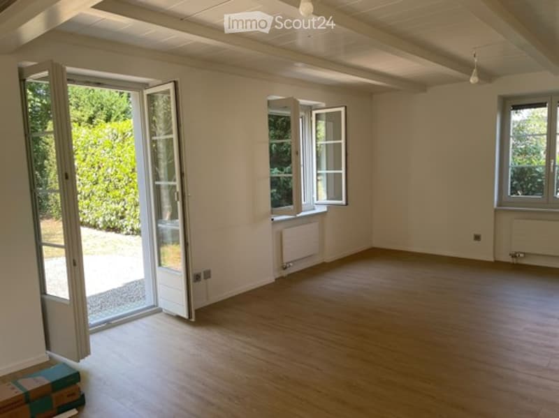Empty room with wooden flooring, white walls, large windows, and a sliding glass door leading to an outdoor area.