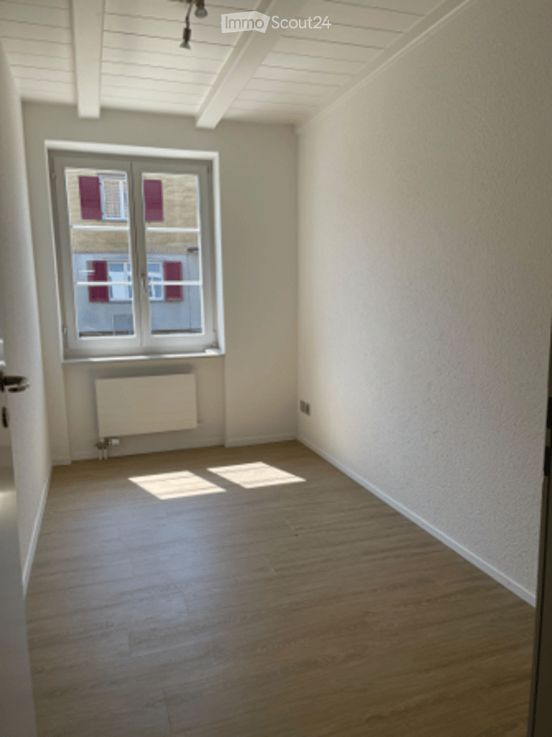 Empty room with wooden flooring, white walls, and a single window with a radiator below it. No furniture or equipment present.