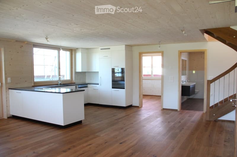 Bright, open-plan kitchen and bathroom area with white cabinets, a central island, and wooden flooring. The kitchen features a sink, faucet, and oven, while the adjacent bathroom includes a sink and toilet.