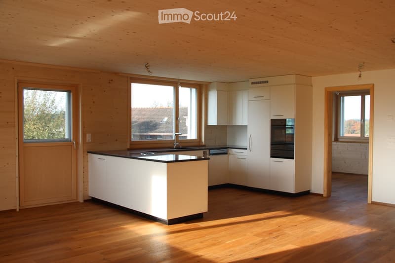 Modern kitchen with white cabinets, a central island, and wooden flooring. Features include a sink, faucet, and an oven.