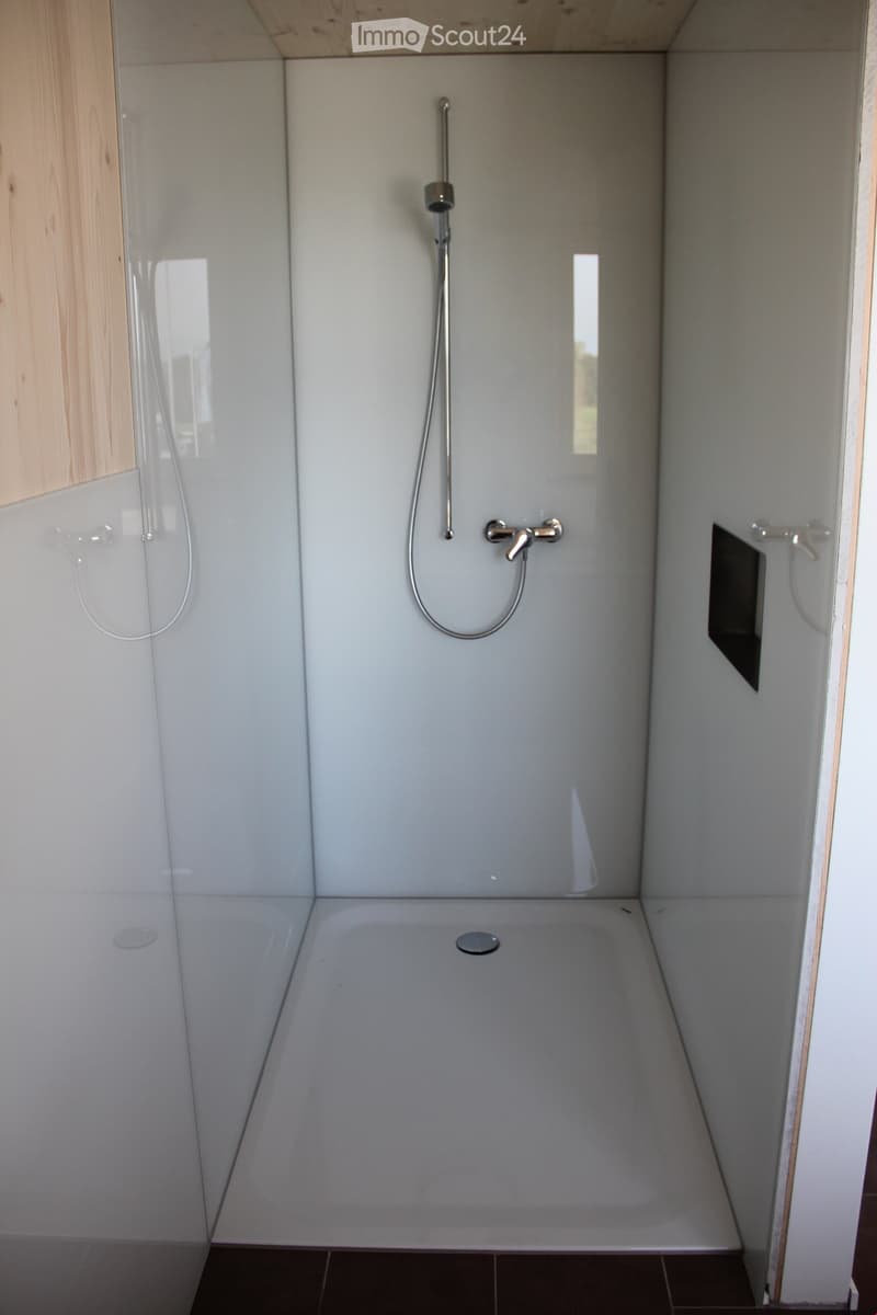 Modern bathroom with a large bathtub, a handheld showerhead, and a sleek faucet. The walls are white, and the floor is tiled in dark brown.