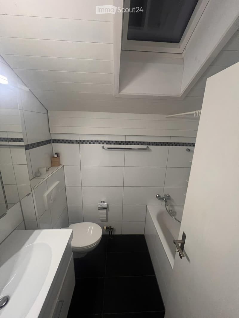 Modern bathroom with white tiles, black floor, bathtub, toilet, sink, mirror, and towel rack.