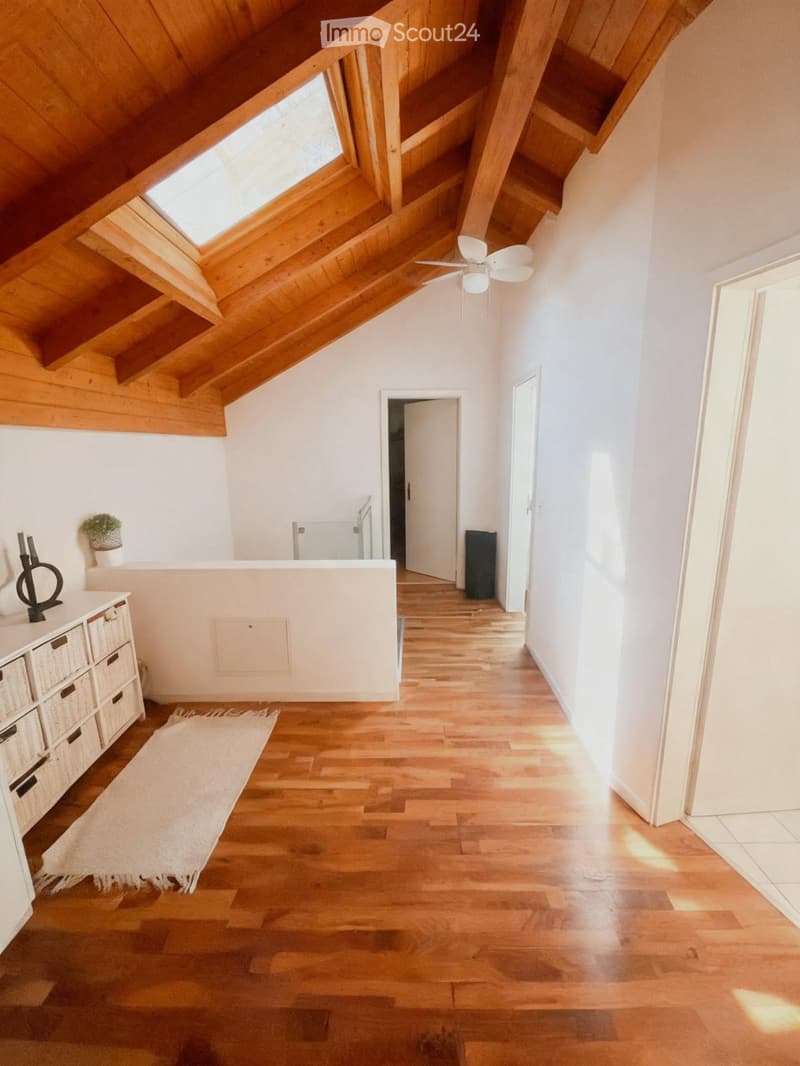 Bright hallway with wooden flooring, white walls, and a skylight. Features a small white cabinet with woven baskets, a white rug, and a potted plant on a shelf.