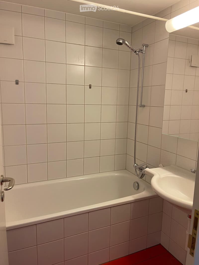 Bathroom with a white bathtub, a white sink, a showerhead, and tiled walls and floor.