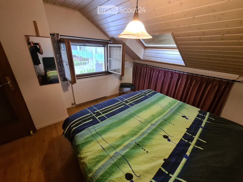 Cozy attic bedroom with wooden floors, slanted ceilings, large windows, and a colorful bedspread.