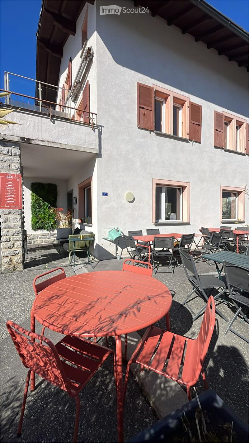 Outdoor seating area with red tables and chairs, attached to a building with shutters and a balcony.