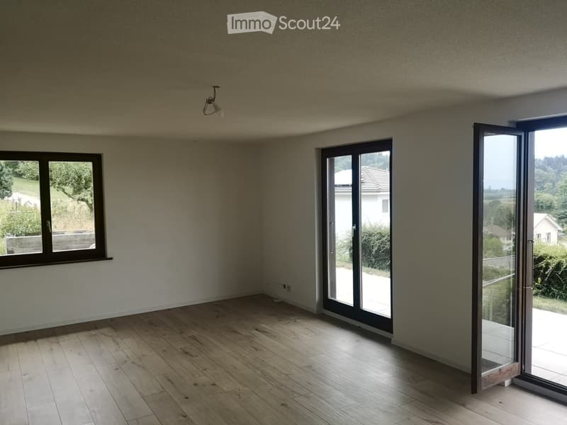 Empty room with wooden flooring, large windows, and sliding glass doors leading to a balcony or outdoor area.