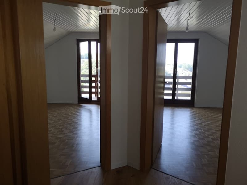 Empty room with wooden flooring, large windows, and a slanted ceiling. No furniture or equipment present.