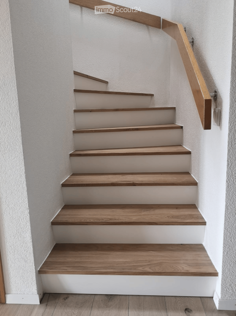 A modern staircase with wooden steps and a matching wooden handrail, set against white walls.