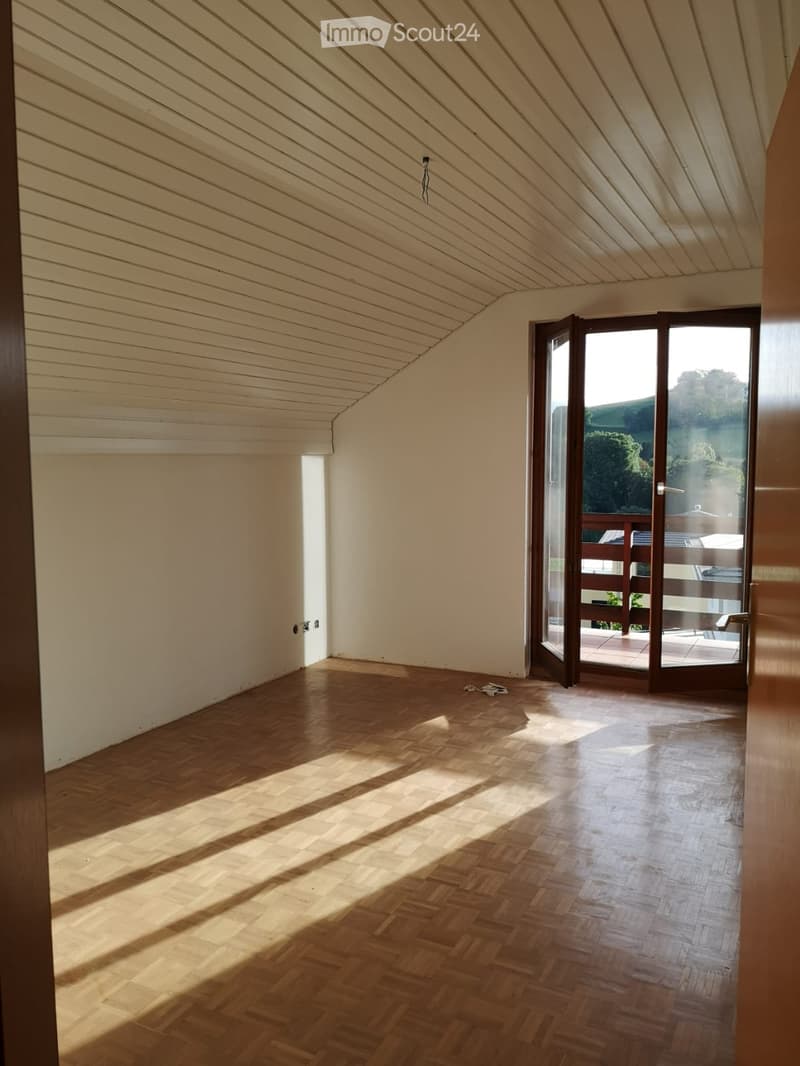 Empty room with wooden flooring and large windows, leading to a balcony or terrace area.