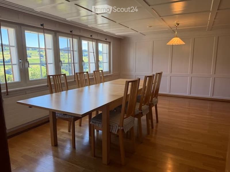 Bright dining room with large windows offering a scenic view, featuring a wooden dining table and matching chairs.