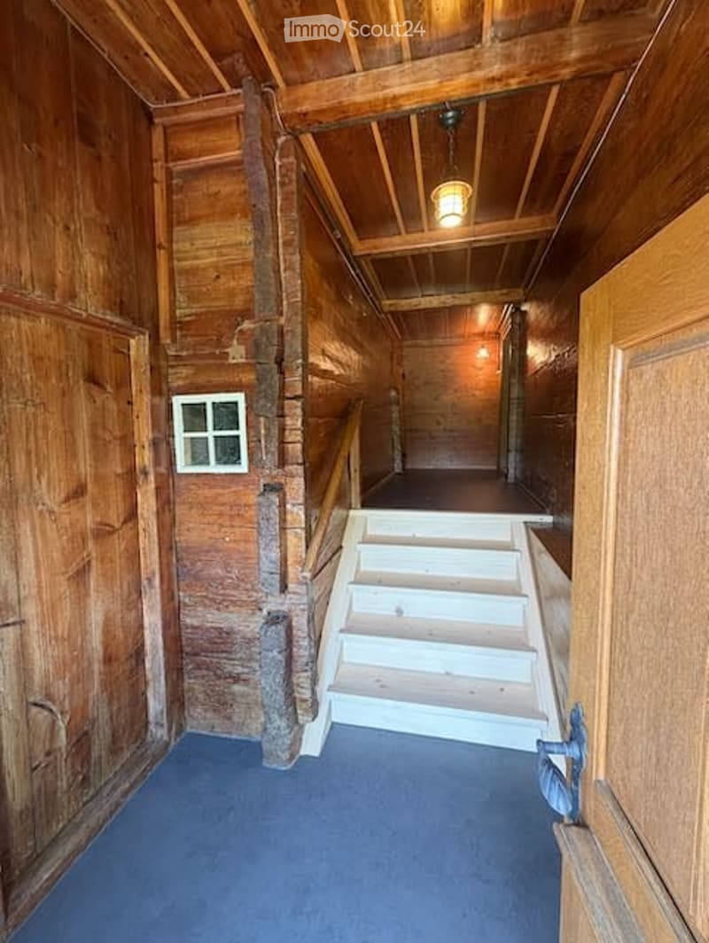 Wooden hallway with exposed beams, blue carpet, small window, and staircase leading upwards.