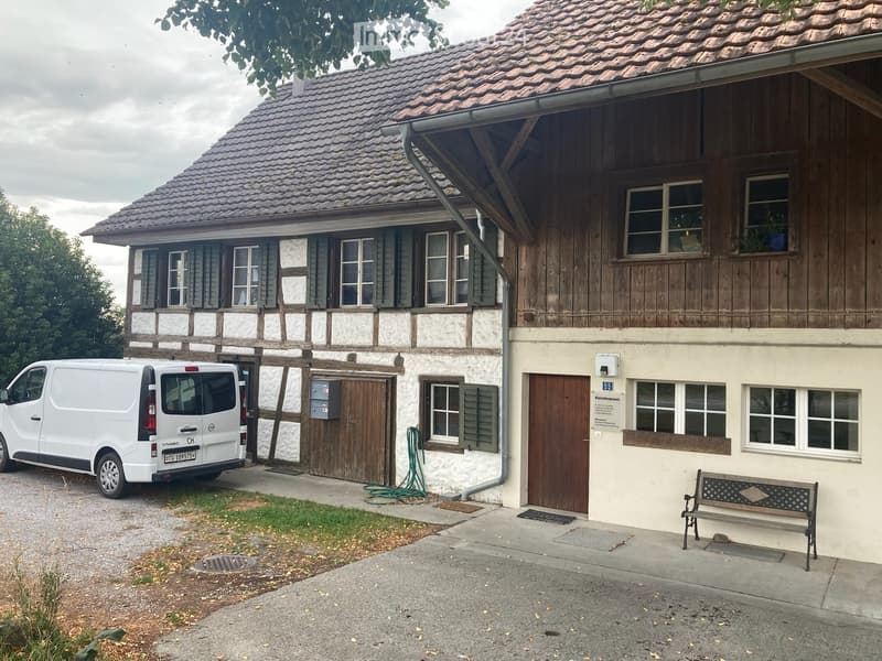 Two-story traditional house with wooden facade, tiled roof, multiple windows, and a parked van in front.