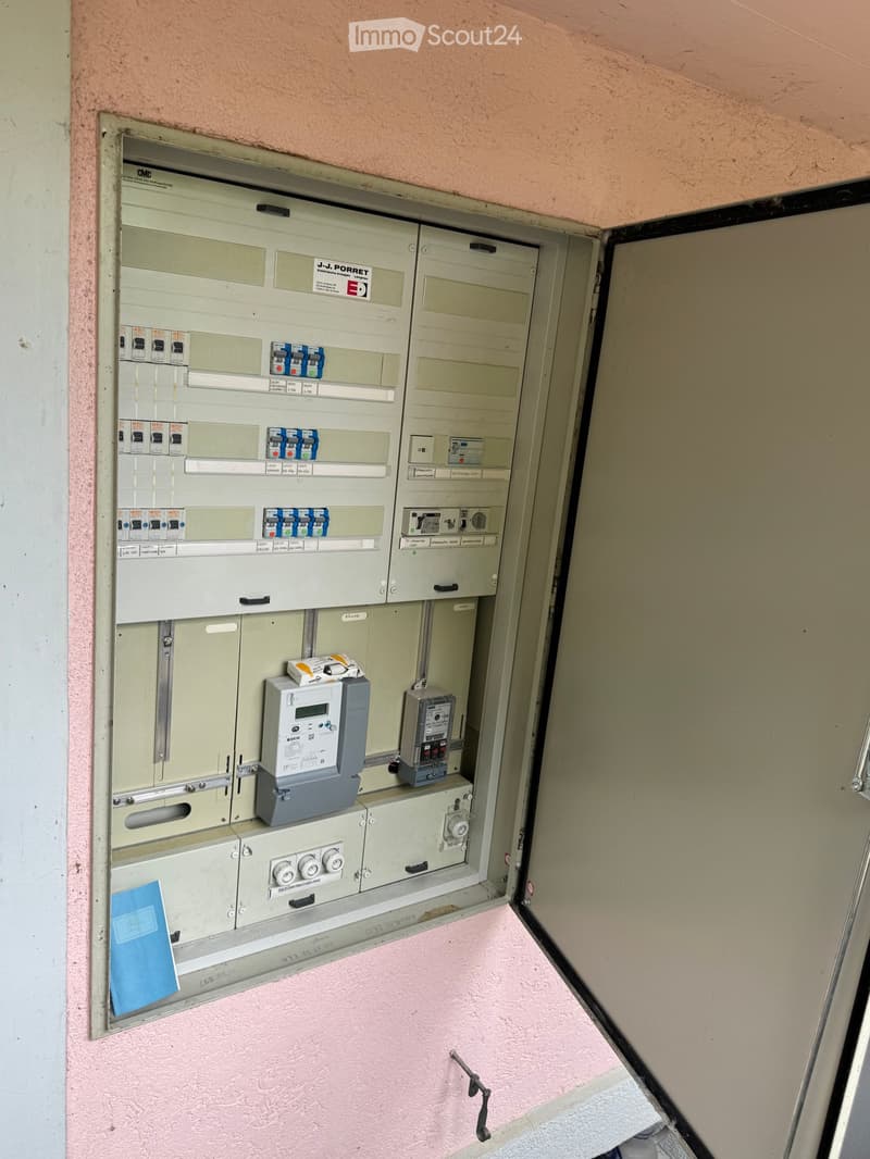 Open electrical panel with multiple switches, meters, and wiring components mounted on a pink wall.