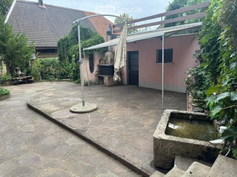 Outdoor patio area with stone flooring, umbrella stand, small fountain, and surrounding greenery.