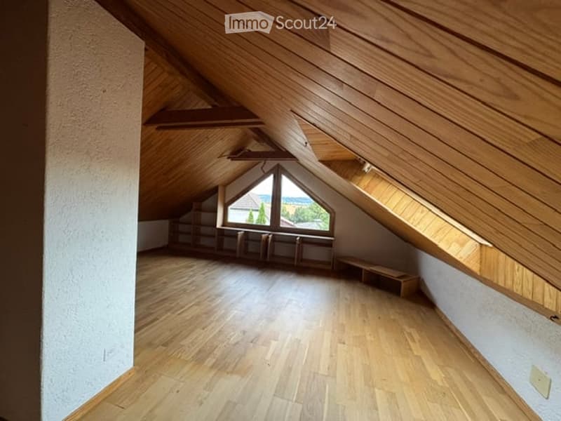 Empty attic room with wooden slanted ceilings, wooden flooring, and a large skylight window offering a view of the outdoors.
