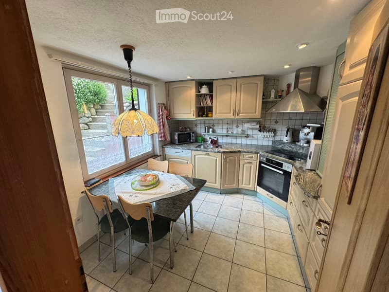 Bright kitchen with cream-colored cabinets, granite countertops, and a dining area with a table and chairs. Features include a microwave, oven, and a hanging lamp.