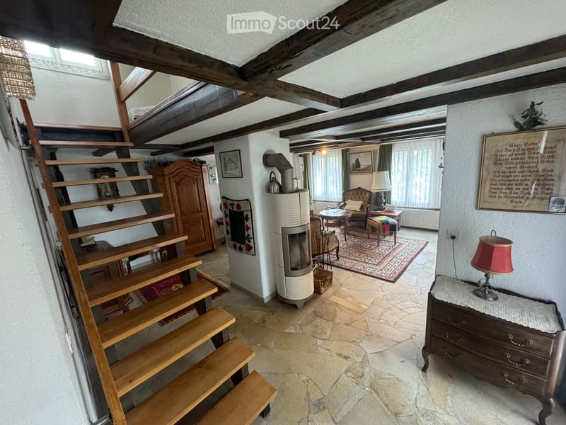Cozy living room with exposed wooden beams, stone flooring, staircase, fireplace, sofa, table, and chairs.