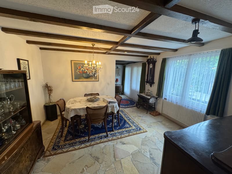 Dining room with exposed wooden beams, a chandelier, a dining table with chairs, a cabinet, and a clock on the wall.