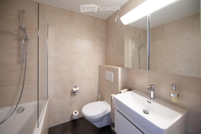 Modern bathroom with a white sink, toilet, bathtub, and glass-enclosed shower. Features a large mirror with built-in lighting and a sleek chrome faucet.