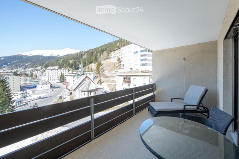 Balcony with a scenic mountain view, featuring a lounge chair, a glass table, and a wicker chair.