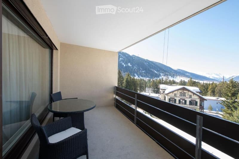 Balcony with a scenic mountain view, featuring a round glass table and wicker chairs.