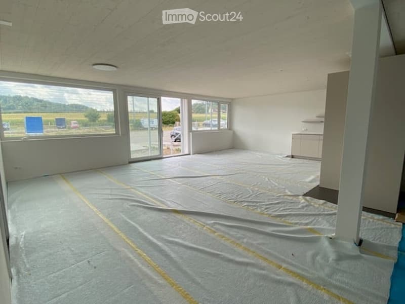 Empty room with large windows, white walls, and a protective floor covering. No furniture or equipment present.